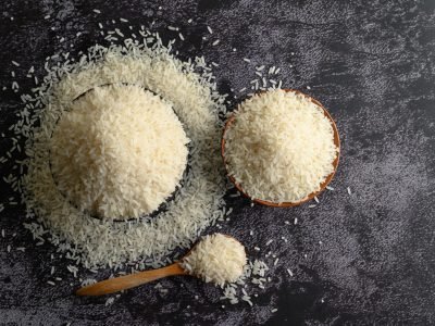Milled rice in a bowl and a wooden spoon on the black cement flo Milled rice in a bowl and a wooden spoon on the black cement floor. Top view